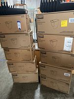 Stacked cardboard boxes of Rubbermaid 2950 side bins in a warehouse setting. Multiple boxes showing brand and quantity labels.