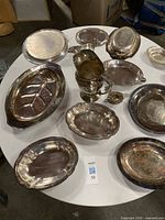 Twelve assorted silver-plated serving pieces arranged on round table