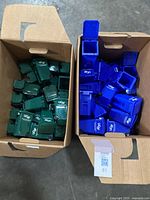 Two cardboard boxes filled with miniature trash bins. Left box contains green bins; right box contains blue bins with UCSF branding.