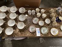 Wide top-down view of multiple tea cups, saucers, and plates arranged on marble surface, showing various floral and gold decorative patterns.