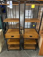 Two matching wood and metal framed shelving units with four wooden shelves and one drawer each, standing on a concrete floor.