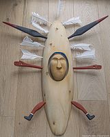 Front view of the hand carved wooden mask showing carved face, feathers and painted accents