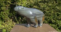 Front-right side view of soapstone polar bear sculpture on wood surface outdoors showing multicolor banded stone
