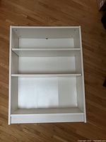 Front view of the white IKEA Billy bookcase showing three shelves, laying flat on the floor.