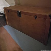 Front view of the cedar chest showing the rectangular shape, wood grain texture, and brass fixtures attached at the front.