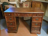 Front view of antique hardwood desk showing seven drawers with brass handles, top surface and leg details.