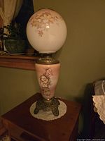Full view of the 1920s oil lamp converted to electric, showing floral glass globe and base with ornate metal stand.