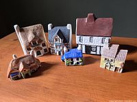 Photo shows six miniature English country houses made of ceramic or pottery, each about 3 inches tall with various traditional English architectural styles and colors.