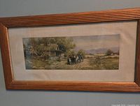 Framed vintage landscape print showing a countryside scene with house, people, and fields, mounted on linen and enclosed in a gold-tone wooden frame.