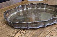 Silver plate gallery tray with scalloped edges and pierced gallery rim, shown resting on wooden table.