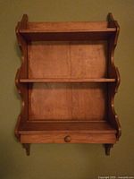 Maple stained hardwood wall-mounted display shelf featuring two shelves and a bottom drawer with wooden knob, decorative curved sides, measuring 18 x 30 inches.