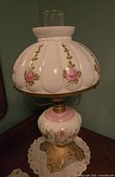 Converted oil lamp with white scalloped glass shade featuring pink rose floral patterns, matching floral decorated base on ornate brass stand, modern clear glass chimney on top.
