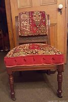 Front view of 1870s antique parlour chair showing patterned upholstery, tufted seat front, turned wood legs with casters, and wooden frame backrest with matching fabric.