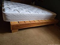 Side angle photo of the pine wood bed frame holding a white spring mattress, showing the frame's slatted base and mattress quilting detail.