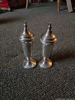 Pair of vintage silver plate salt and pepper shakers placed on carpet showing their full height and design details.