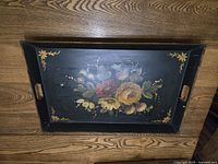 Top down view of rectangular toleware tray, black with hand-painted central floral design and corner yellow flowers, showing cut-out handles on sides.