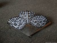 Photo of Victorian lady's fan showing patterned black, white, and gray leaf with wooden ribs and original string holder at the base