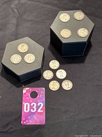 Photo showing 12 Canadian silver quarters arranged on black hexagonal holders with additional coins laid in front and a purple tag with number 032.