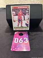 Hockey card of Guy Lafleur held upright showing full card front art and text, with card resting on a black display stand and numbered tag below.