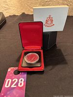 Coin in red velvet-lined black presentation case, shown with outer white and black box with Canadian crest.