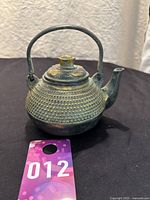 Front side view of brass teapot showing the textured dotted surface and arched handle with short curved spout