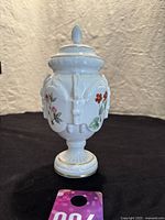 Full front view of the white porcelain tea caddy jar with floral decoration and lid displayed upright on a black surface, showing overall shape and height.