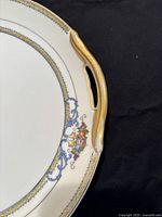 Close-up image of cake plate handle showing gold gilt decoration and floral pattern near rim.