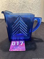 Side view of cobalt blue glass creamer pitcher showing chevron pattern and spout.