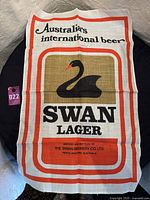 Full view of vintage Swan Lager linen tea towel with brand logo, border and text visible.