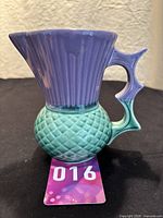 Full front view of the ceramic thistle jug showing purple ribbed upper spout, green textured body, and detailed handle.