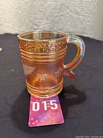 Full view of the Imperial Glass carnival glass mug in smoke color showing embossed lettering around the top and star designs on the body.