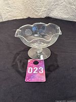 Full view of clear glass bowl with ruffled edge and pedestal base on black background