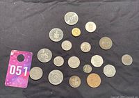 Collection of nineteen assorted world coins and tokens on a dark cloth background.