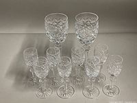 Front view of all 10 Waterford crystal glasses arranged standing on a surface; 2 large and 8 small glasses grouped.