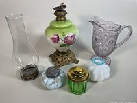 Antique floral milk glass kerosene hurricane lamp with green uranium glass humidor, milk glass containers, glass pitcher, and sugar shaker arranged together