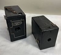Two Butcher's Carbine No. 3 box cameras side by side on white surface, showing front and side views