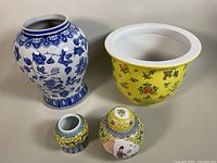 Four porcelain items arranged with the blue and white vase, famille jaune bowl planter, and two smaller jars in front.