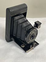 Three images showing the Kodak Model B vest pocket folding camera from various angles, highlighting the front lens plate, folding bellows, and original leather case.