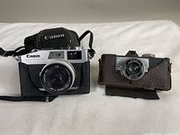 Two vintage 35mm film cameras side by side: Canon Canonet 28 and Universal camera with respective cases.
