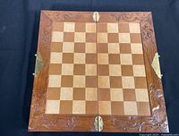 Top view of chessboard showing checkered playing surface and carved wooden frame with brass hinges.