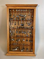 Full view of wood wall display case with multiple rows of assorted collectors spoons arranged inside