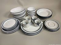 Photo showing the entire set comprising bowls, cups, saucers, and plates arranged on a flat surface, displaying the consistent blue stripe around rims and very good condition.