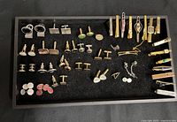 Full view of tray with assorted men's cufflinks and tie clips laid out on black felt.