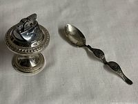 Photo showing full lot: sterling silver weighted table lighter with beaded edges and pedestal base next to a 5.75 inch sterling silver collectors spoon with decorative handle.