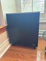 Advent subwoofer enclosure in black woodgrain finish with logo badge on front and small feet beneath.