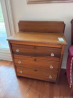 Front view of antique wooden dresser with a raised backboard, three drawers with clear glass knobs, and dovetailed drawer construction.