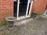 Both urns side by side in front of brick wall and door