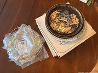 Top view of Russian fairy tale themed decorative plate with vibrant colors and gold detailing on black background with plate stands and boxes underneath on wooden table.