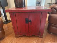 Front view of red distressed wooden cupboard with latch and scalloped bottom edge.