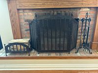 Wrought iron fireplace screen, log holder, and tool stand set arranged in fireplace.